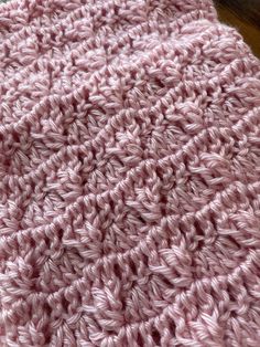 a pink crocheted blanket laying on top of a wooden table