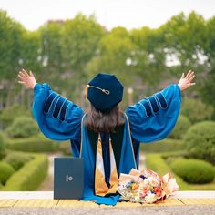 a graduate sitting on the ground with her arms outstretched