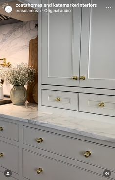 a kitchen with white cabinets and marble counter tops, gold pulls on the handles in front of an oven