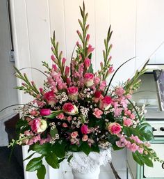 a white vase filled with pink flowers and greenery