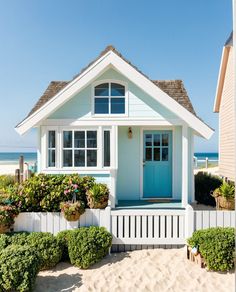 a blue door sits in front of a white house on the beach with shrubs and flowers