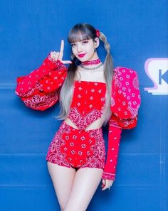 a woman with long hair wearing a red top and matching shorts poses in front of a blue wall