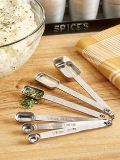 six measuring spoons with herbs on them sitting next to a bowl of mashed potatoes