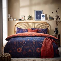 a bed with an orange and blue comforter in a bedroom next to a window