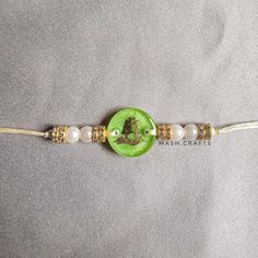 a green and white beaded bracelet with a button on the clasp that says mash crafts