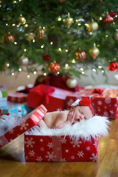 a baby is laying in a christmas present under a tree with presents on the floor