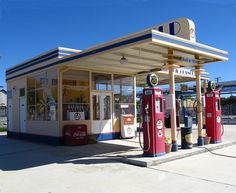 an old fashioned gas station with two red and white pumps on the side of it