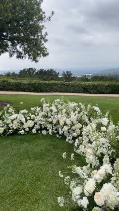 a circular arrangement of white flowers on the grass in front of a tree and bushes