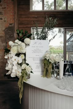 a table topped with white flowers and greenery next to a sign that reads the menu