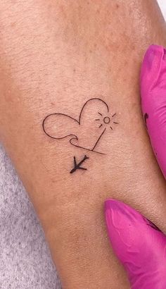 a woman's arm with a small heart and an arrow tattoo on the wrist