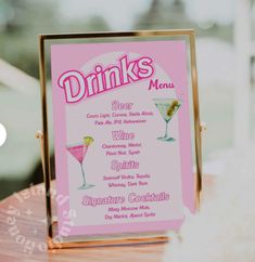 a pink menu sign sitting on top of a wooden table next to a glass filled with drinks