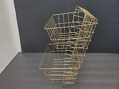 a golden wire basket sitting on top of a gray floor next to a white wall