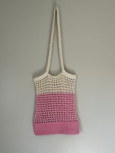 a pink and white crocheted bag hanging on a wall