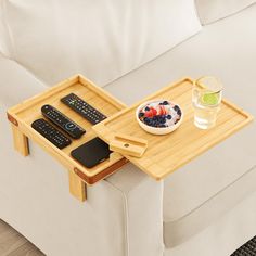 a tray with remotes and a bowl of fruit on it sitting on a couch