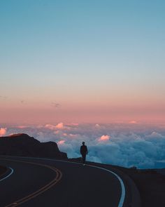 a person standing on the side of a road with clouds in the sky behind them