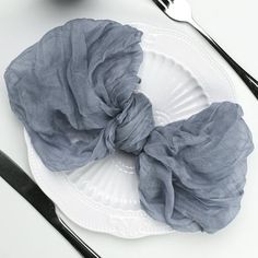 a white plate topped with a gray scrunch on top of it next to utensils