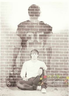 a man sitting on the ground in front of a brick wall with a statue behind him