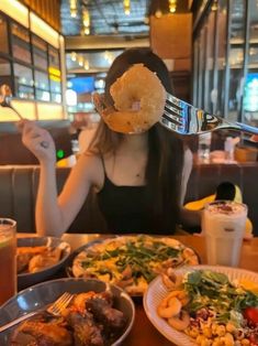 a woman sitting at a table with plates of food in front of her and a fork sticking out of her face