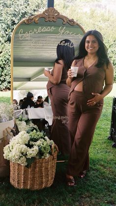 two women standing next to each other in front of a sign with flowers on it