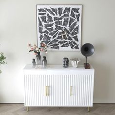 a white cabinet sitting in front of a painting and vases on top of it