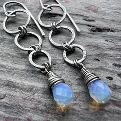 These long dangle earrings are handmade from sterling silver and Opalite. The small Opalite teardrops are wrapped in sterling silver. Above the teardops are a set of rings which I have formed, soldered, and hammered by hand. The earrings dangle from handmade sterling silver earwires. The silver has been oxidized and polished to create an antique patina finish.Be sure to see all photos and video for size and color reference.Opalite: About 5x7mmTotal Earring Length: Just over 2 inchesTotal Earring Nickel Free Briolette Teardrop Earrings In Sterling Silver, Nickel-free Briolette Teardrop Sterling Silver Earrings, Unique Teardrop Sterling Silver Earrings, Handmade Sterling Silver Long Drop Teardrop Earrings, Handmade Sterling Silver Teardrop Pendant Earrings, Modern Wire Wrapped Teardrop Jewelry, Modern Teardrop Wire Wrapped Jewelry, Silver Teardrop Jewelry With Hand-wrapped Detail, Unique Hand Wrapped Silver Earrings