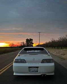 a white car is parked on the side of the road as the sun goes down