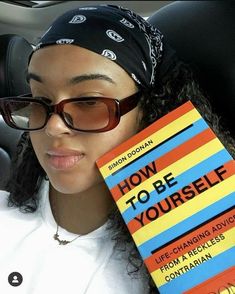 a woman sitting in the back seat of a car holding up a book that says how to be yourself