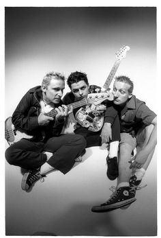 three men are sitting together with guitars