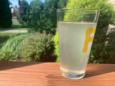 a glass filled with water sitting on top of a wooden table next to a window