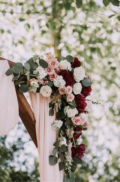 a wedding arch with flowers and greenery hanging from it's sides in front of trees