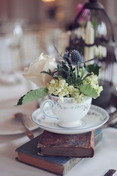 a tea cup with flowers in it sitting on top of a stack of old books