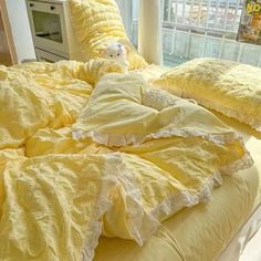 an unmade bed with yellow comforter and pillows on it in front of a window