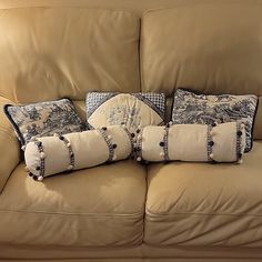 three pillows are placed on the back of a tan couch with blue and white accents