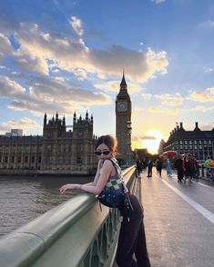 a woman standing on the side of a bridge next to a clock tower at sunset