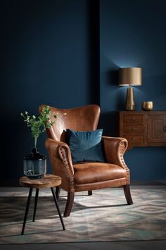 a brown chair sitting in front of a blue wall next to a table with a potted plant on it