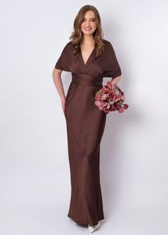 a woman in a brown dress is holding a bouquet and posing for the camera with her hands on her hips