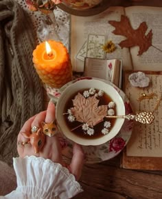 a woman holding a cup of coffee with an orange candle in it and some other items on the table