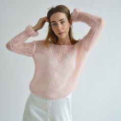 a woman in a pink sweater and white skirt posing for the camera with her hands on her head