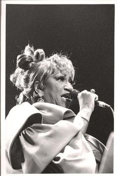 a black and white photo of a woman singing into a microphone with her hair in a bun