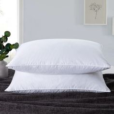 two white pillows sitting on top of a bed next to a vase with a plant