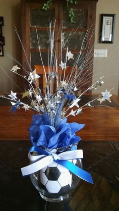 a soccer ball and star decoration in a glass vase on a table with blue ribbon