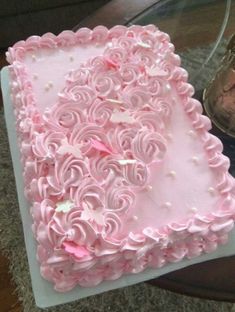 a pink heart shaped cake sitting on top of a white plate next to a glass vase