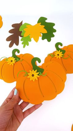 a hand holding an orange paper cutout with fall leaves and pumpkins on it