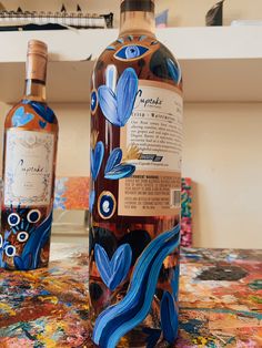 two bottles of alcohol sitting on top of a table next to each other and one bottle has blue flowers painted on it