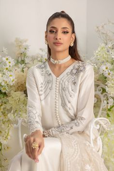 Effortlessly chic- An Eid Must have , cut from Pure ivory raw silk, the neckline & sleeves features an intricate zardozi work in silver, glistening sequins & 3D floral work, Front open with loop button details for a monochromatic look. Statement eyelet embroidered dupatta finished with lace trim and hand- crafted tassels completes the minimal yet elegant look of this outfit. Shirt & pants Fabric: Pure 80gms Raw Silk Shirt Length: 52” (customisable, mention in order notes) Dupatta Fabric: Pure Em Kurti Long, White Silk Dress, Zardozi Work, Designer Outfit, Floral Work, Pants Fabric, Embroidered Dupatta, Fabric Designs, Pakistani Designers