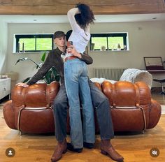 a man and woman standing on top of a couch in a living room next to each other