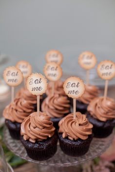 chocolate cupcakes with brown frosting and small wooden signs on top are sitting on a glass plate