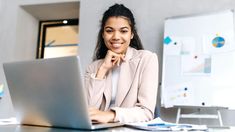 a woman sitting at a desk with a laptop computer in front of her, smiling