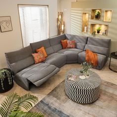 a living room with a sectional couch and coffee table in the middle, surrounded by potted plants