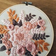 a close up of a embroidery on a wooden surface with flowers in the center and leaves around it